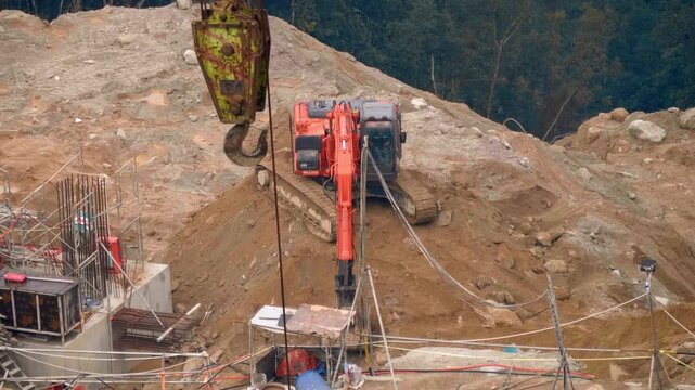 A red crawler excavator operating at a construction site is moving excavated earth to another location
