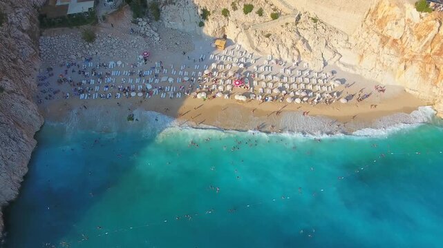 Aerial Kaputas Beach in Kas Antalya Turkey shows turquoise water, cliffs, umbrellas, and crowds.