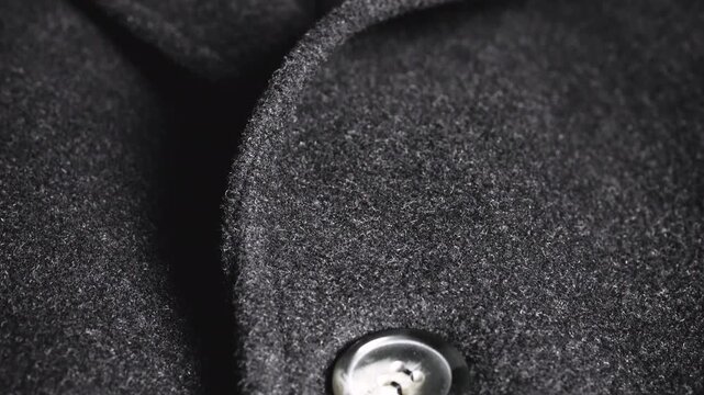 A close-up of a dark grey wool coat lapel shows high-quality winter apparel fabric, elegant black buttons, tailoring craftsmanship, professional textile weaving, and classic clothing design.