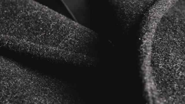 An extreme close-up of vintage horn buttons on a dark grey wool coat captures textured winter jacket fabric catching dramatic light, revealing rich patterns and classic outerwear quality material.