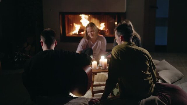 Friends Gather Around Fireplace While Guitarist Plays by Candlelight