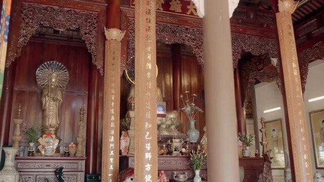 An altar with gilded bronze statue of Buddha Shakyamuni sitting in the meditation posture with vases and lotus flowers in front of the altar. Hai Duc Buddhist Institute located on Trai Thuy Hill 