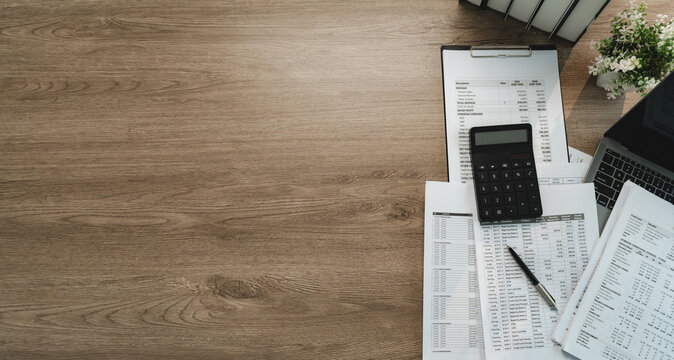 Accounting workspace with calculator, financial reports and laptop on wooden desk with wide copy space, showing accounting analysis, bookkeeping and business finance planning.