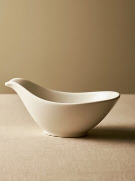 Empty white ceramic gravy boat on a textured beige surface with copy space