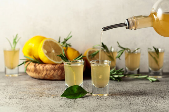 Italian liqueur Limoncello with fresh lemons and rosemary branches on a gray stone table.