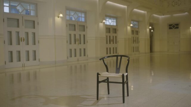 Single black chair standing alone in a bright elegant white hall with soft natural light