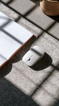 Wireless computer mouse and notebook on a grey felt desk mat with natural light
