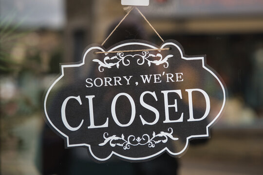 Hanging closed sign on a glass storefront door, signaling a temporary or permanent shop shutdown and reflecting retail closure, economic strain, or a quiet, empty local street scene