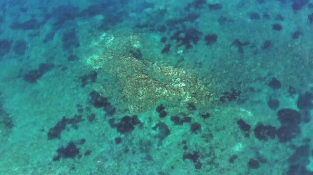 Aerial drone overhead of submerged rock and seamount in Chile with shallow turquoise water.