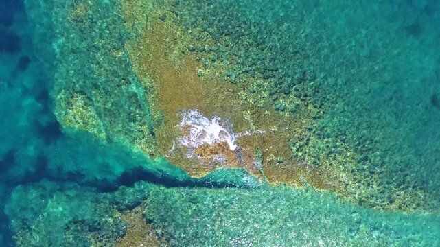 Aerial drone overhead of submerged rock and seamount in Chile with shallow turquoise water.