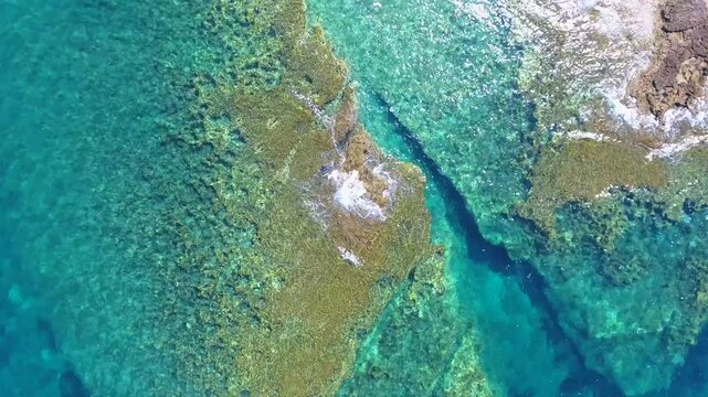 Aerial drone overhead of submerged rock and seamount in Chile with shallow turquoise water.