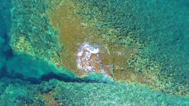 Aerial drone overhead of submerged rock and seamount in Chile with shallow turquoise water.