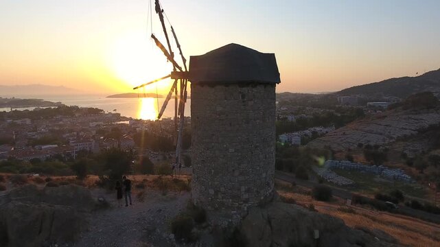 Aerial drone view of a historic stone windmill on a dry hill in warm Mediterranean light.