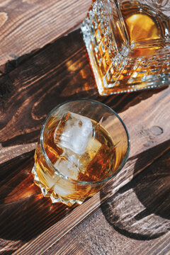 Amber rum with ice cubes in a glass on a wooden background