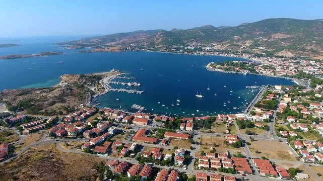Aerial drone view of Foca harbor in Izmir Turkey with marina, boats, houses, and Aegean bay.