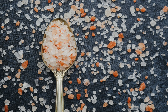 Pink Himalayan salt crystals scattered on a dark background with a spoon full