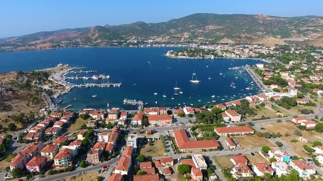 Aerial drone view of Foca harbor in Izmir Turkey with marina, boats, houses, and Aegean bay.