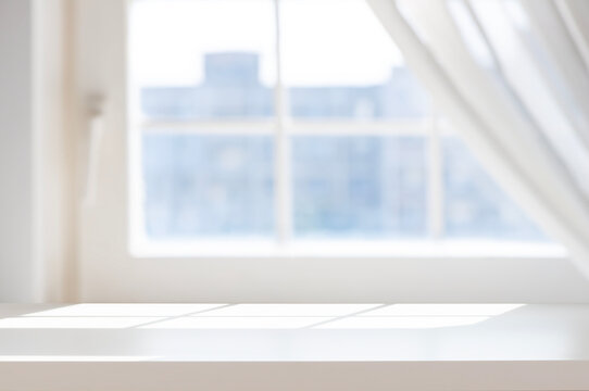 Empty white table top with blurred window background and curtains