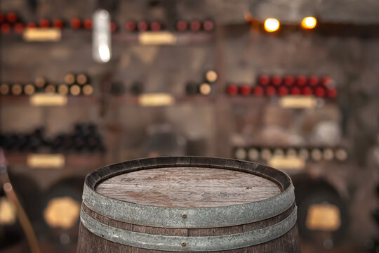 Wooden wine barrel as empty podium in a blurred wine cellar with wine racks and bottles