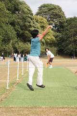 Obraz premium Cricket player bowling on a green pitch during an outdoor match, capturing dynamic action, focus and athletic motion as the bowler delivers the ball in competitive team play