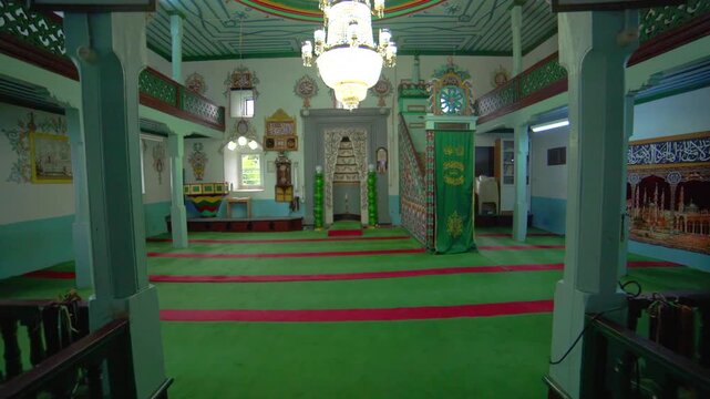 Historic wooden mosque interior with mihrab, carpet, and Islamic prayer hall without people.