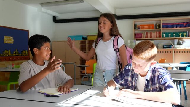 Two male students concentrating on their classwork at their desks while a female classmate arrives and begins to mock and bully them in a sunlit classroom, creating a tense atmosphere