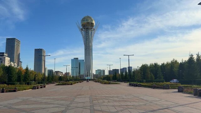Baiterek Monument from Nurzhol Boulevard, capturing tall white structure, golden sphere, city buildings and bright summer sky, Nur-Sultan, Kazakhstan, shot handheld, 4k footage