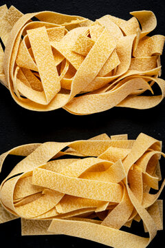 Italian food dry pasta carbohydrate ready for cooking. Close up view with raw pappardelle ribbons on textured black background. Authentic culinary gastronomy concept for healthy eating lifestyle.