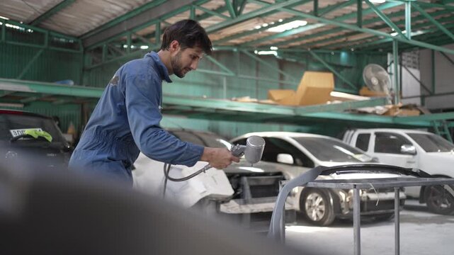 Mechanic Spray Painting Primer On Gray Car Bumper In Garage
