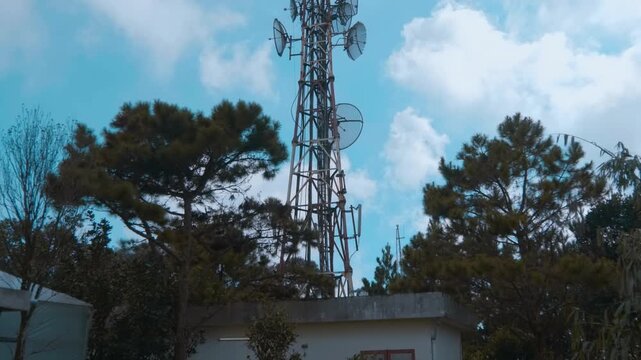 A large telecommunications and broadcasting lattice tower with multiple antennas that sits on the mountain peak in the center against the background of a blue cloudy sky
