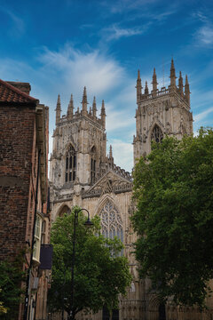 Iconic english gothic cathedral facade standing tall between green trees and old brick buildings under a blue sky, representing history, architecture, and tourism