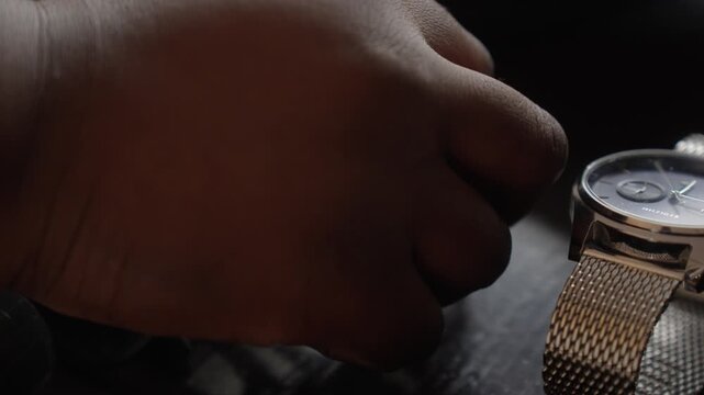 Close-up of a groom preparing his accessories, touching a cufflink or monogram detail on a wooden table during wedding preparations in Brittany, France.