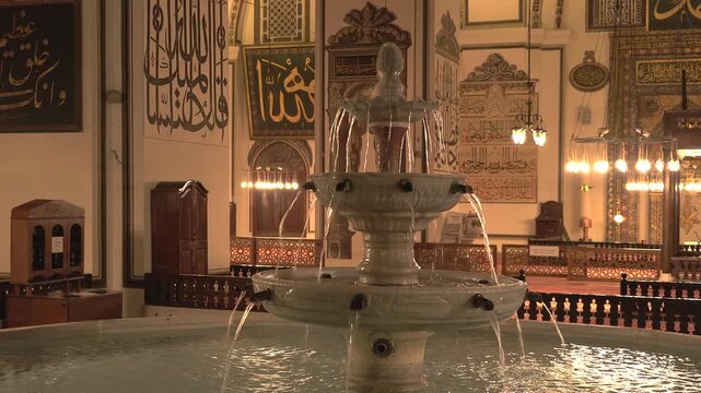 Bursa Turkey mosque fountain pool reflects warm night lights inside quiet sacred architecture.