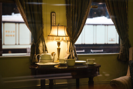 Luxurious vintage train interior featuring a traditional porcelain tea set, a warm glowing lamp, and green curtains, offering a cozy view outside the carriage window