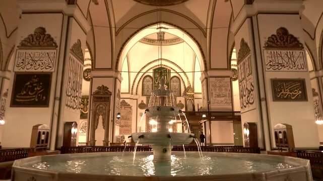 Bursa Turkey mosque fountain pool reflects warm night lights inside quiet sacred architecture.