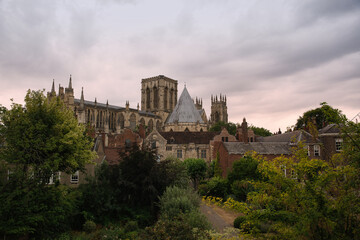 York minster cathedral stands tall above traditional buildings and lush green trees, creating a timeless architectural landscape under a soft, cloudy sky in yorkshire, england © Fotografia Juan Reig
