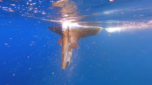 Underwater footage shows a boat propeller and rudder below a vessel near the water surface.