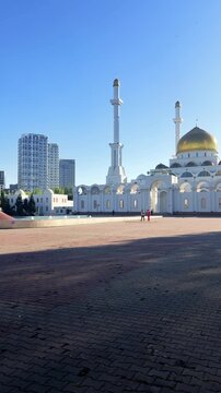 Abu Nasr Al-Farabi Mosque against clear blue sky, capturing golden dome, elegant minarets, white facade and open public plaza, Astana, Kazakhstan, shot handheld, vertical video, 4k footage