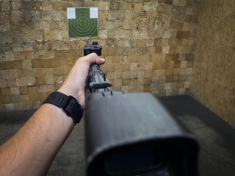 First person view aiming a tactical rifle with laser sight at a target in an indoor shooting range