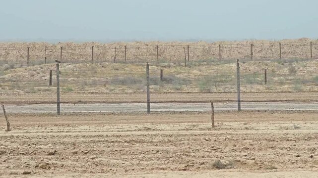 Turkmenistan border fence crosses a dry empty frontier landscape with repeating barbed wire.