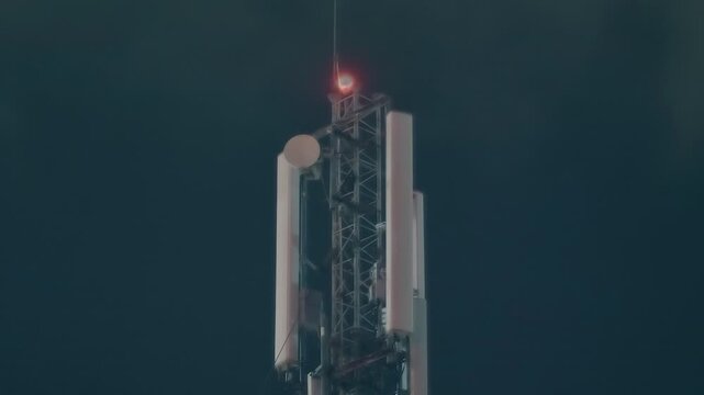 A tall telecommunication tower with steel lattice framework typically used for cellular or wireless communication signals with mounted antennas and a flashing red warning light at the top 