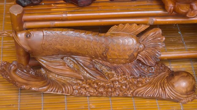 A polished red wooden carving of an Asian arowana (also known as a dragon fish) resting on a textured base that represents water waves. Shot in motion
