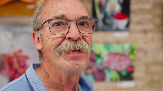 A close up of a senior man with glasses and a mustache talking animatedly inside an art gallery, Slow Motion.