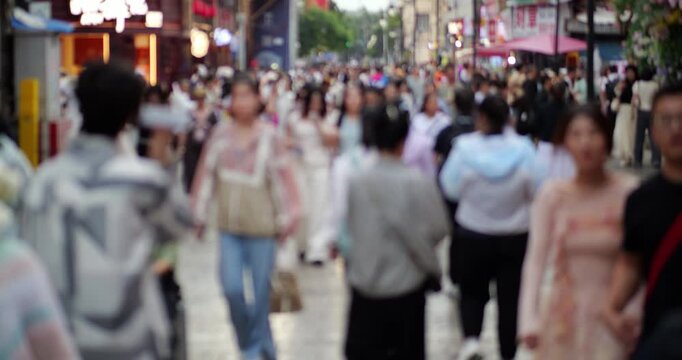 Defocused lengthwise medium telephoto view of anonymous people walking along historic Guanghua Street in downtown Kunming, with families, couples, friends, and small groups strolling past