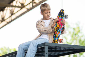 Cute blonde boy with a skateboard looking contented and enjoyed © zinkevych