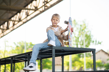 Cute blonde boy with a skateboard looking contented and enjoyed © zinkevych