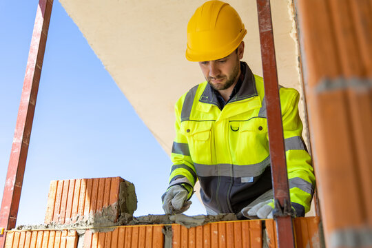 Male mason wearing helmet applying cement mixture with trowel