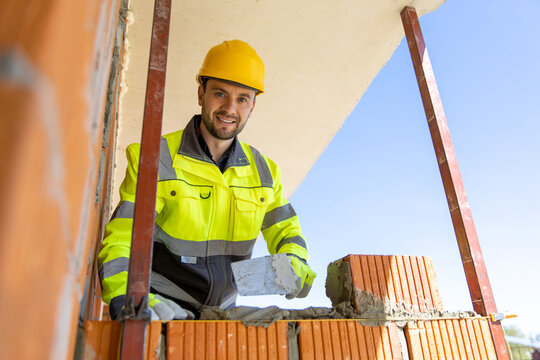 Smiling constructor wearing safety gear holding trowel looking at camera