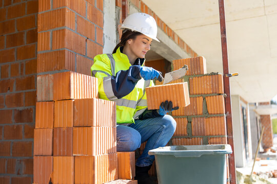 Female construction worker working with trowel and brick