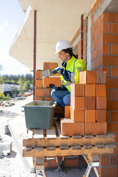 Female construction worker applying mortar on brick with trowel